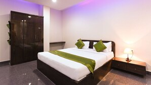 A neatly made bed with a green throw, a bedside lamp, and a dark wooden wardrobe in a hotel room.