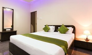 A neatly made bed with white linens and green accents, a bedside table with a lamp, and a mirror on the wall. - Vaishnavi Residency by Urban Hotels  (Bengaluru)