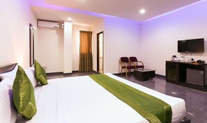 A hotel room with a bed, a desk, a chair, a television, and an air conditioning unit. - Vaishnavi Residency by Urban Hotels  (Bengaluru)