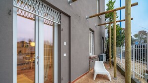 A building with a sliding glass door, a small outdoor seating area with a white plastic chair, and a wooden play structure. - Cascina Conicchio 1 (Brescia)
