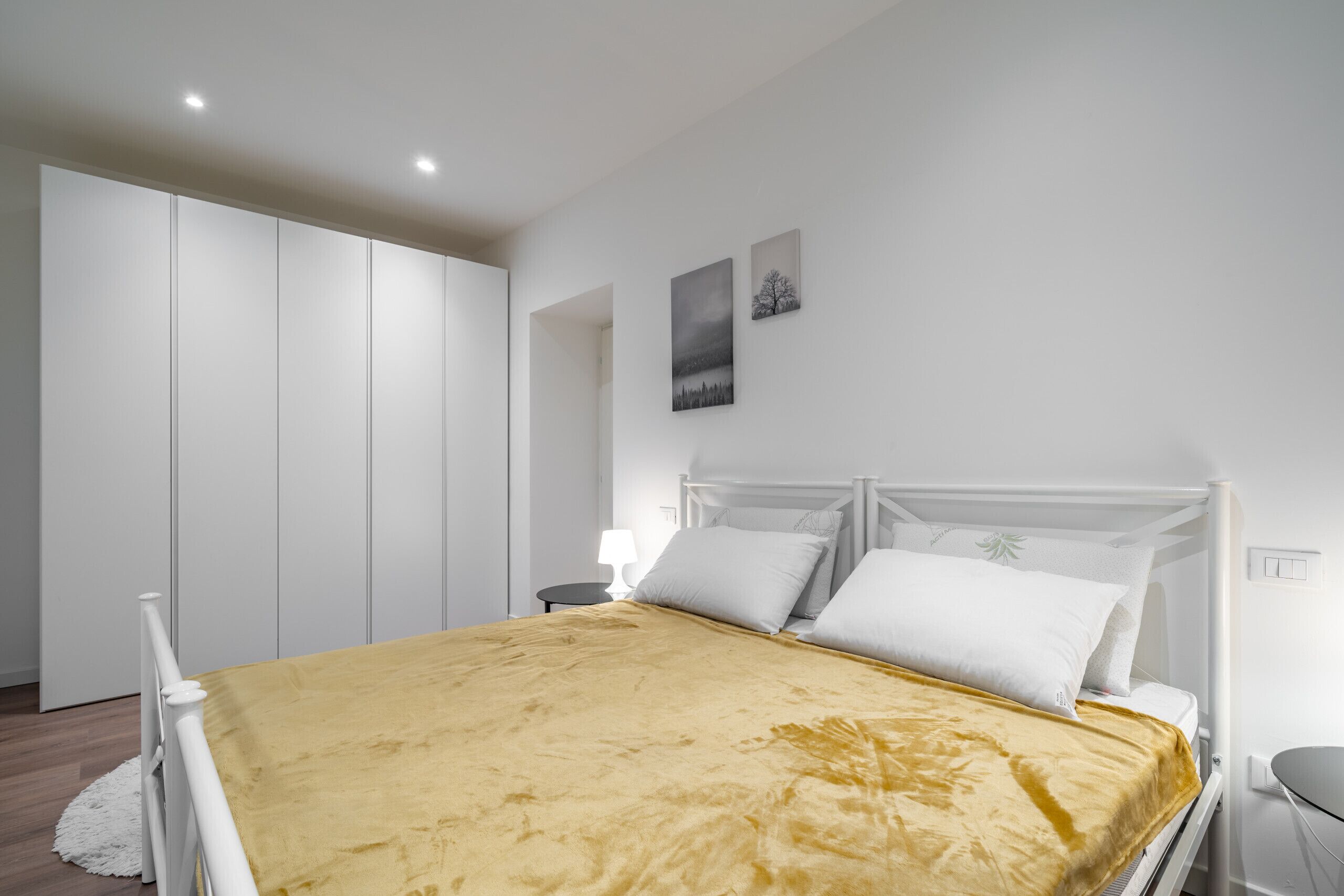 Un dormitorio con una cama, un armario blanco y dos cuadros colgados en la pared.