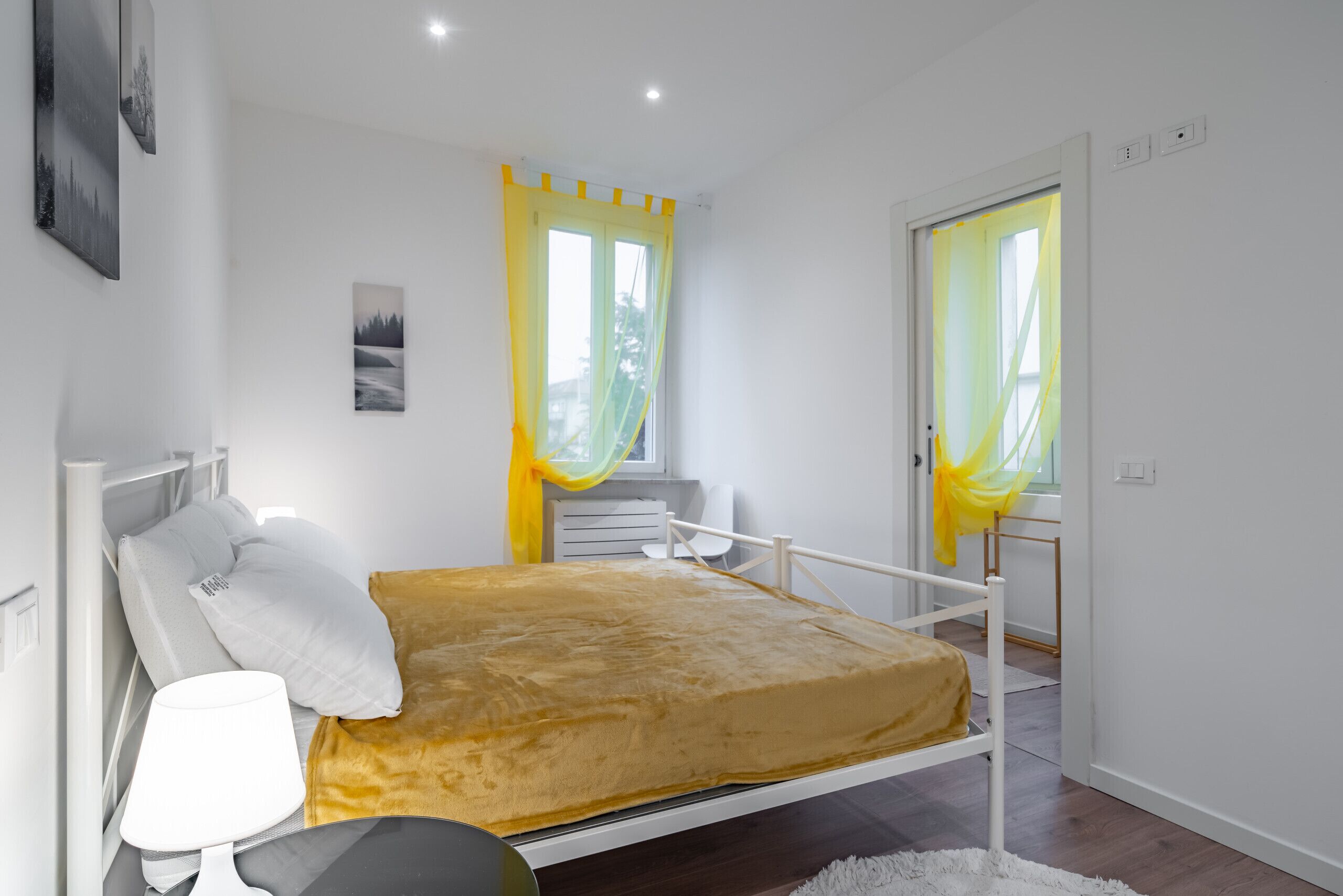 Un dormitorio con una cama, una mesita de noche, una lámpara y una ventana con cortinas.