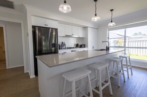 Eine moderne Küche mit weißen Schränken, einem Edelstahlkühlschrank, einer großen Kochinsel mit Barhocker und Pendelleuchten.