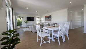 A spacious dining area with a wooden table and white chairs, a sofa, and a TV mounted on the wall. - Luxury on Lesmurdie - Close to Zoo & Golf Club (Dubbo)