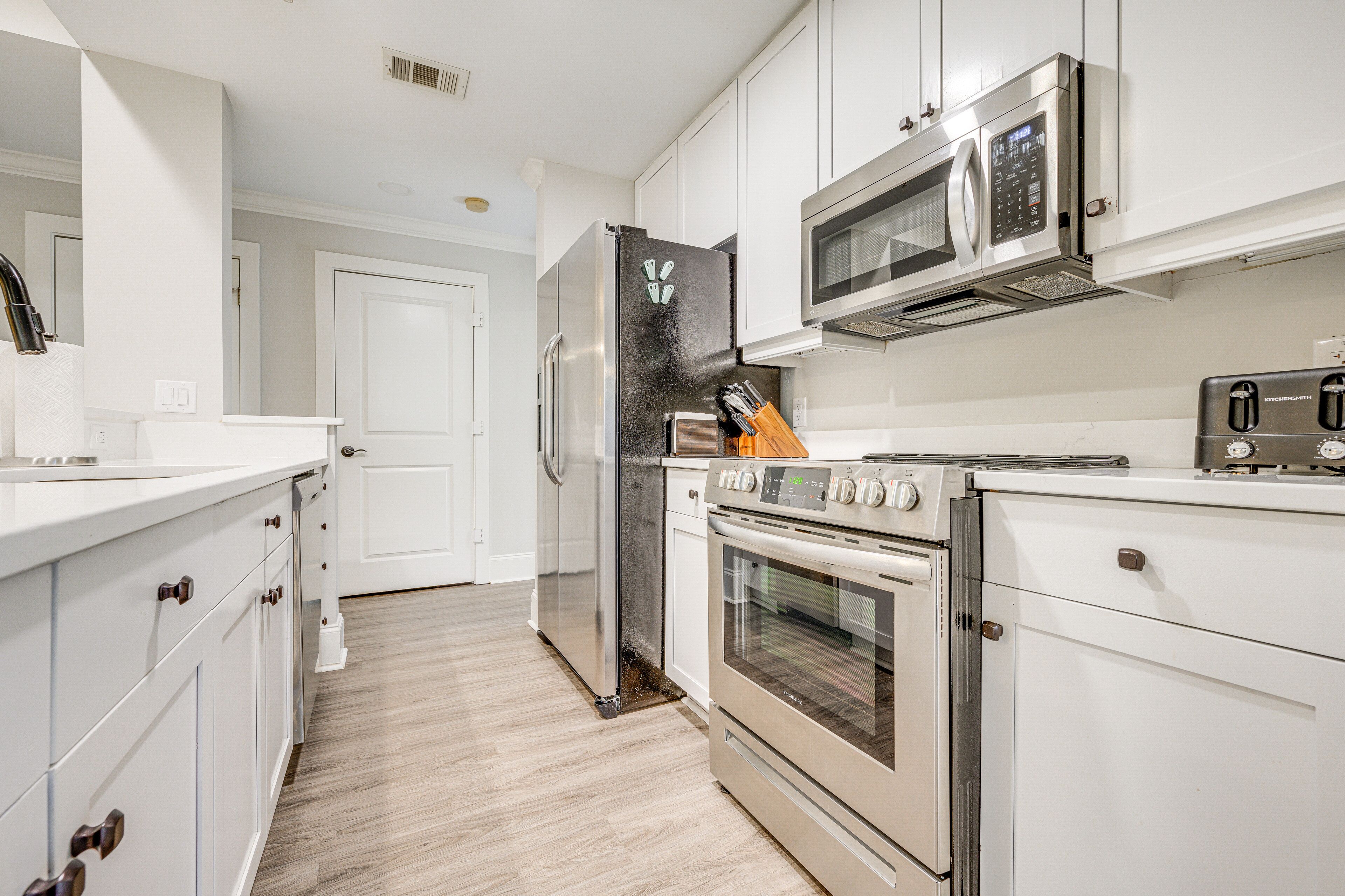 A modern kitchen with stainless steel appliances, white cabinetry, and a wooden floor.
