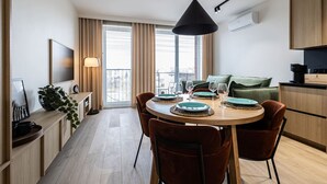 A modern kitchen with a dining area, featuring a round table with chairs, a hanging light fixture, and a view of the city through large windows. - Cuero Centrum Gara Podziemny Dwie Sypialnie (Bydgoszcz)