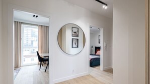 A modern, well-lit room with a round mirror, a dining area with a table and chairs, and a bedroom with a bed and a nightstand. - Cuero Centrum Gara Podziemny Dwie Sypialnie (Bydgoszcz)