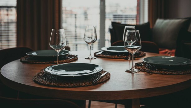 A round dining table with black plates, wine glasses, and a woven placemat. - Cuero Centrum Gara Podziemny Dwie Sypialnie (Bydgoszcz)