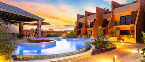 A hotel with a swimming pool, outdoor seating, and a sunset view.