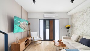 A modern living room with a flat-screen TV, a wooden console table, a white armchair, a round coffee table, and a sofa with a throw blanket. - Minutes to the Beach | Porta Al Sole 10 by Bocobay (Noord)