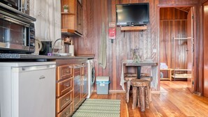 A compact kitchen with a microwave, oven, and washing machine. A flat-screen TV is mounted on the wall above the counter. - Chalet do Relógio d’Água, a Home in Madeira (Ponta do Sol)