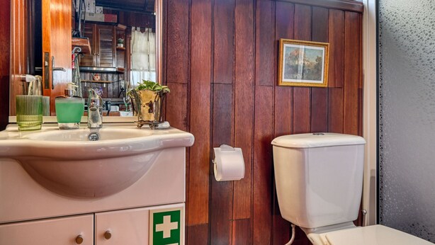 Une salle de bain avec une porte en bois, un lavabo avec un verre vert, des toilettes blanches et un tableau encadré au mur.