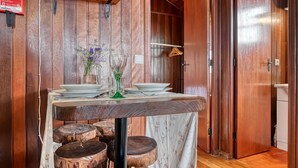 A wooden interior with a dining table set for two, a small vase with flowers, and a wooden stool. - Chalet do Relógio d’Água, a Home in Madeira (Ponta do Sol)