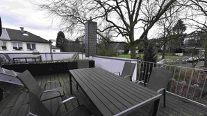 An outdoor deck with a wooden table and chairs, surrounded by a white railing. - Luxuriöse großzügige Wohnung mit 3 Schlafzimmer, Terrasse (Solingen)