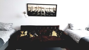 A room with a dark brown sofa, two beds with patterned bedding, a black coffee table, and a framed picture of a cityscape on the wall. - Luxuriöse großzügige Wohnung mit 3 Schlafzimmer, Terrasse (Solingen)