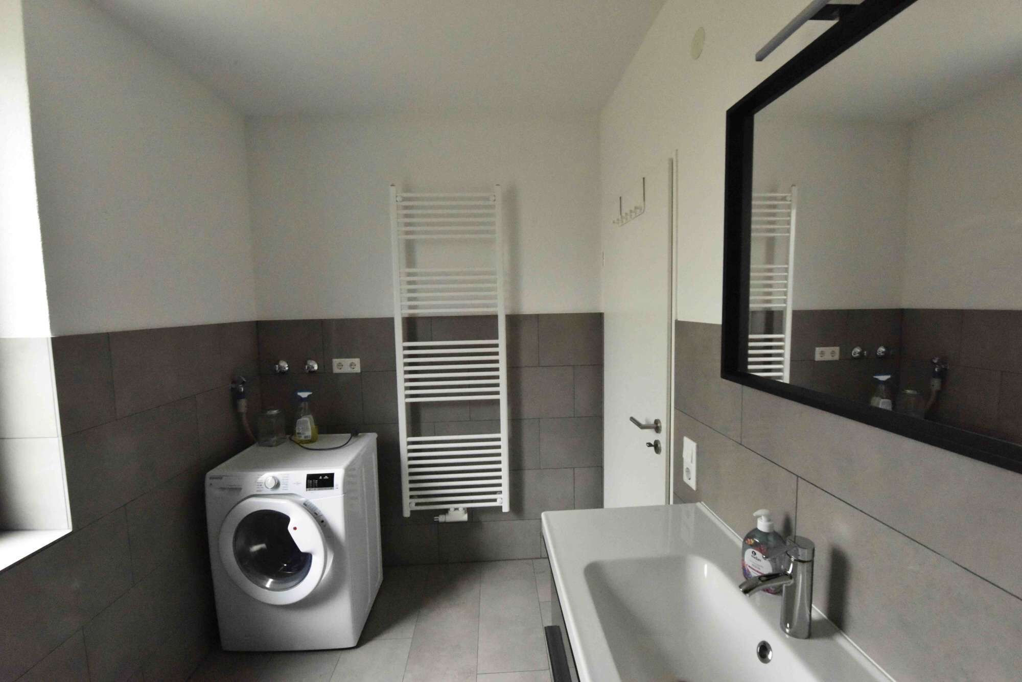 A modern bathroom with a built-in washing machine, a large mirror, and a sink with a faucet.