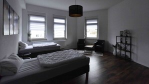 A bedroom with a bed, a desk, two chairs, a hanging light fixture, and a window with blinds. - Luxuriöse großzügige Wohnung mit 3 Schlafzimmer, Terrasse (Solingen)
