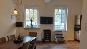 A dining area with a wooden table and chairs, a TV mounted on the wall, and a kitchen area with a refrigerator and oven. - Luxuriöse großzügige Wohnung mit 3 Schlafzimmer, Terrasse (Solingen)