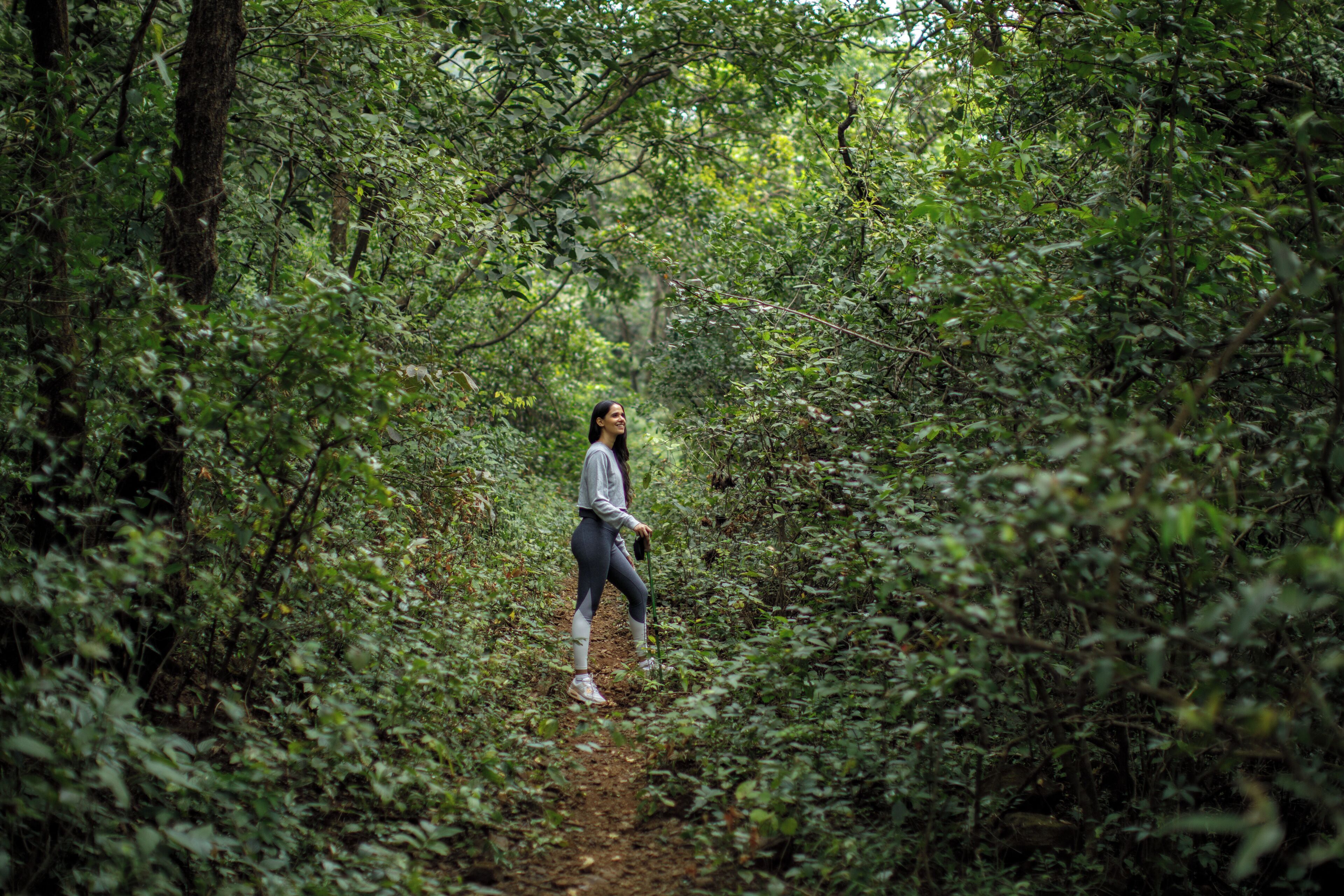 A person walking on a dirt path surrounded by dense green foliage.