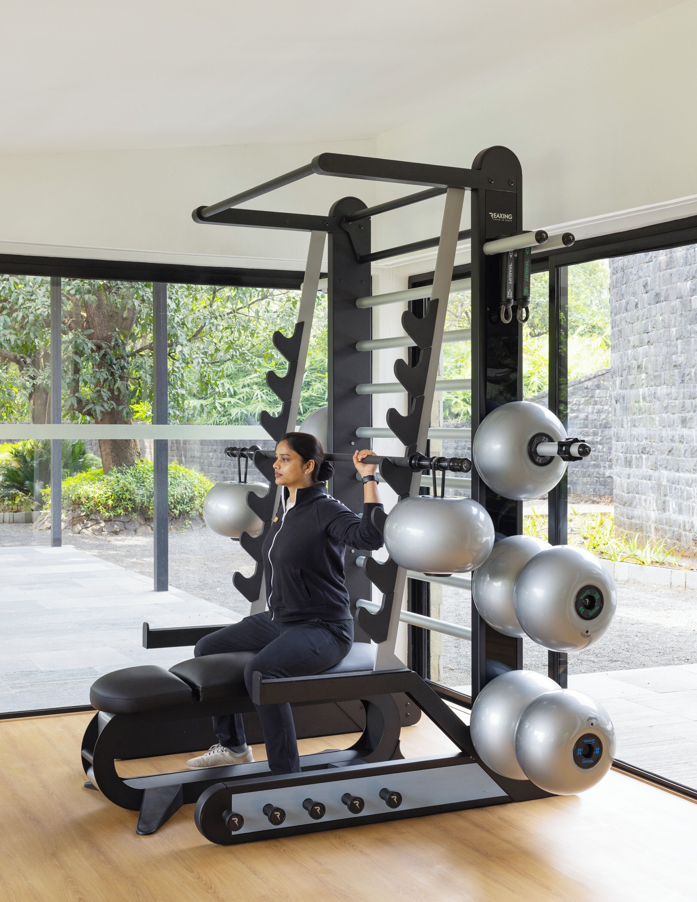 A person using a weight machine in a gym with a view of greenery outside.