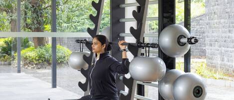 A person using a weight machine in a gym with a view of greenery outside.