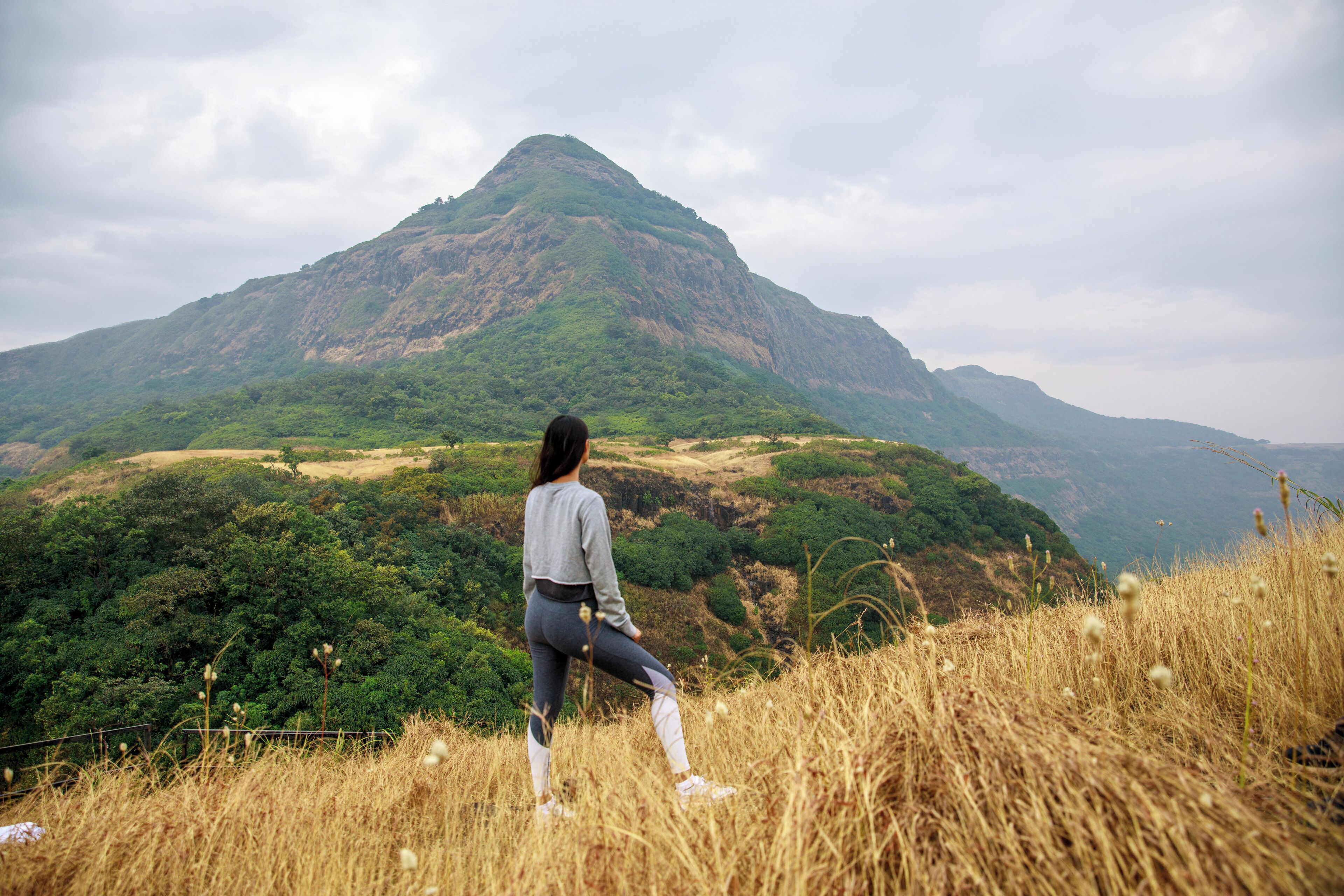 Eine Person steht auf einem grasbewachsen Hügel mit Blick auf eine gebirgige Landschaft.