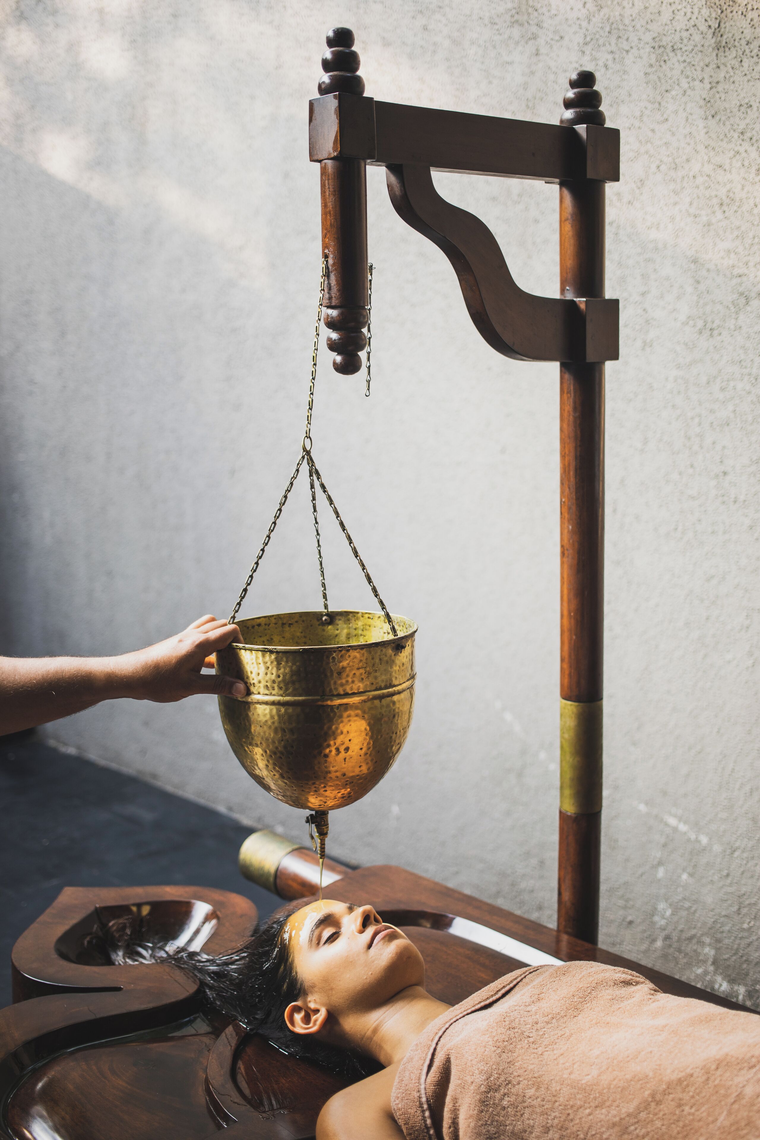 A person receiving a traditional massage with a wooden table and a metal bowl.