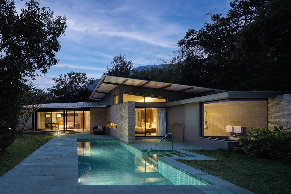 A modern house with a swimming pool, large glass doors, and a well-lit interior.