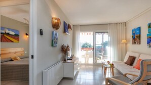 A modern hotel room with a bed, a sofa, a dining table, and a chair. There is a window with curtains, a radiator, and wall-mounted artwork. - Edificio Luxor II by Interhome (Miami Platja)