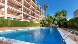 A swimming pool with a metal ladder, surrounded by a hedge and a multi-story building with balconies. - Edificio Luxor II by Interhome (Miami Platja)