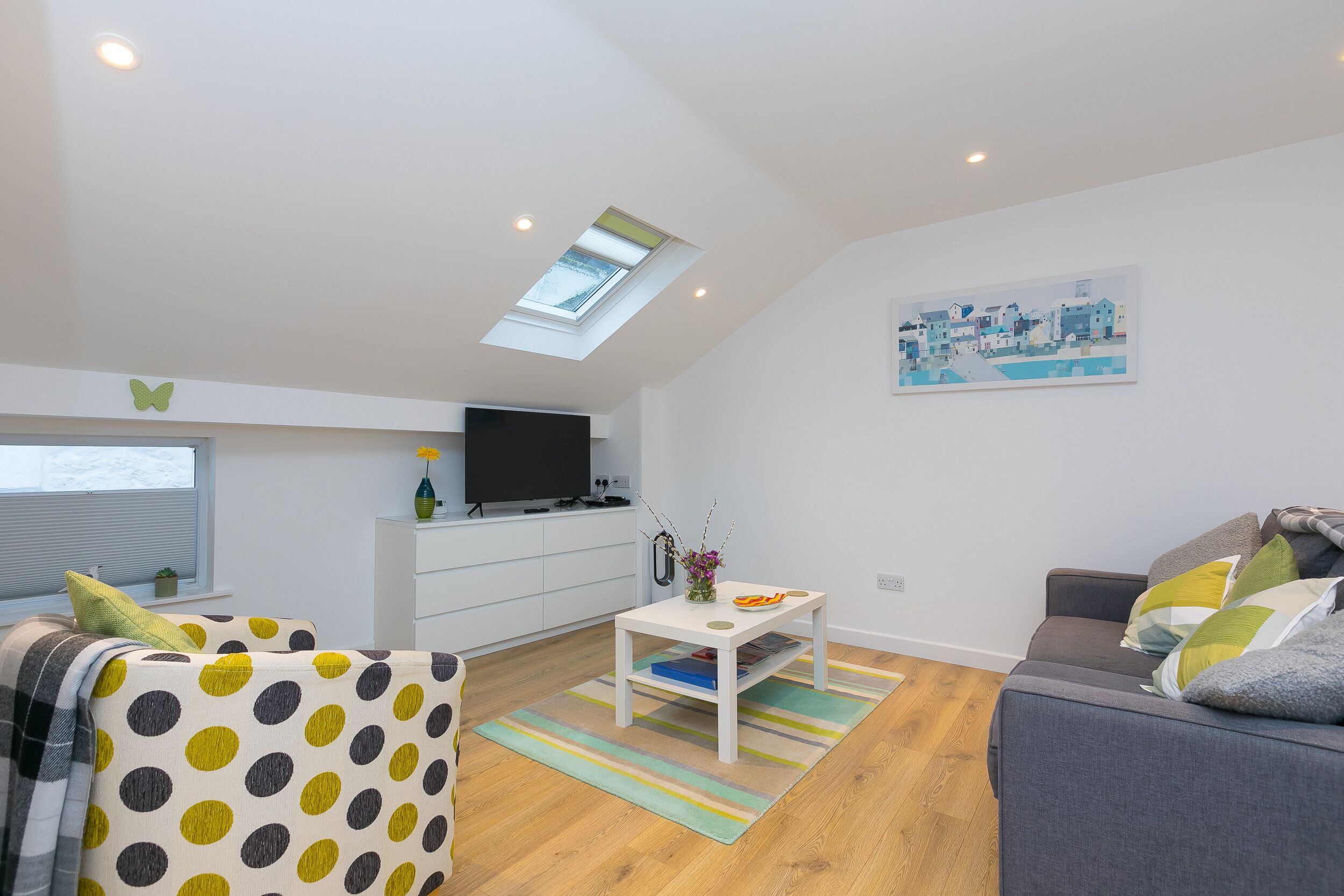 A modern living room with a skylight, a flat-screen TV, a sofa, a coffee table, and a painting on the wall.