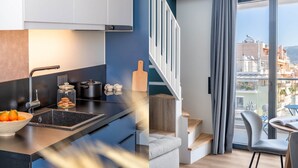 A modern kitchen with a black countertop, a sink, and a bowl of oranges. There is a staircase leading to a balcony with a view of buildings.