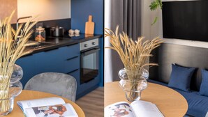 A modern kitchen with blue cabinets, a dining table with a book, and a living area with a sofa and a TV.