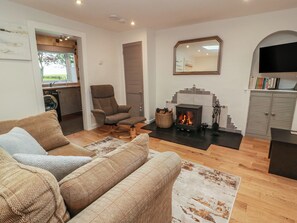 A living room with a sofa, armchair, fireplace, television, and a bookshelf. - Rosalin Cottage (Irvine)