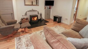 A living room with a fireplace, a sofa, a chair, and a TV. - Rosalin Cottage (Irvine)