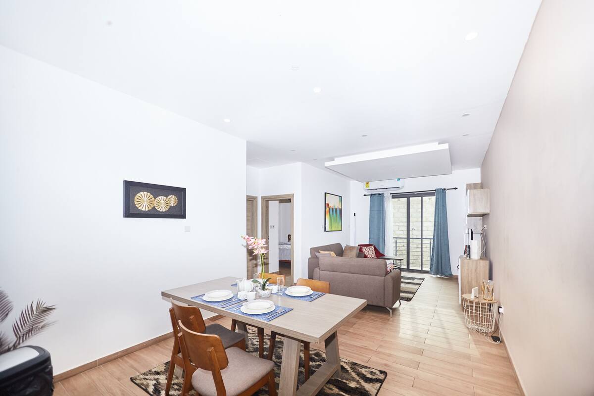 A modern living room with a dining area, featuring a sofa, a coffee table, and a dining table set with plates and chairs.