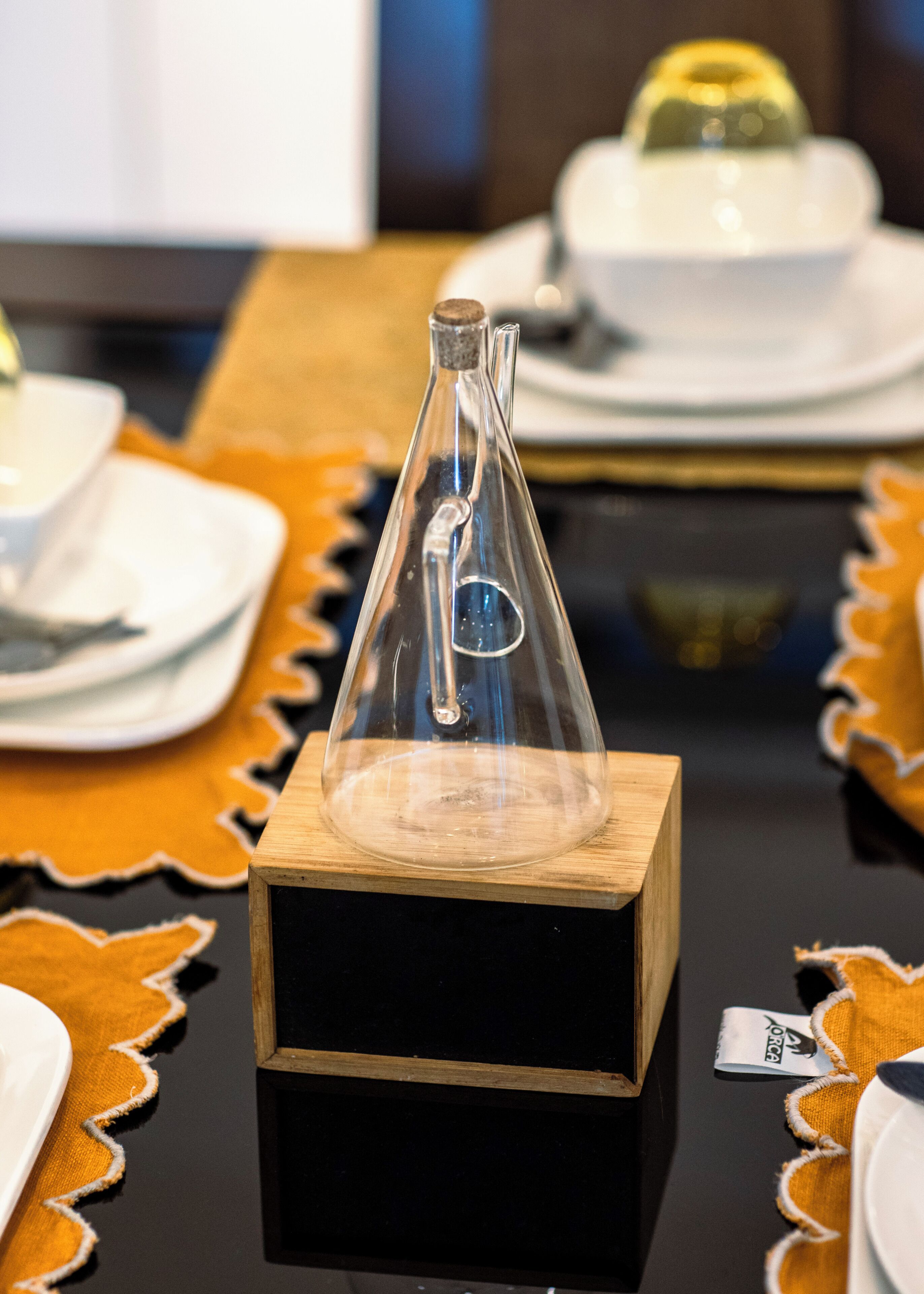 Une bouteille en verre transparent posée sur un bloc de bois, entourée d’assiettes et d’un bol sur une table.