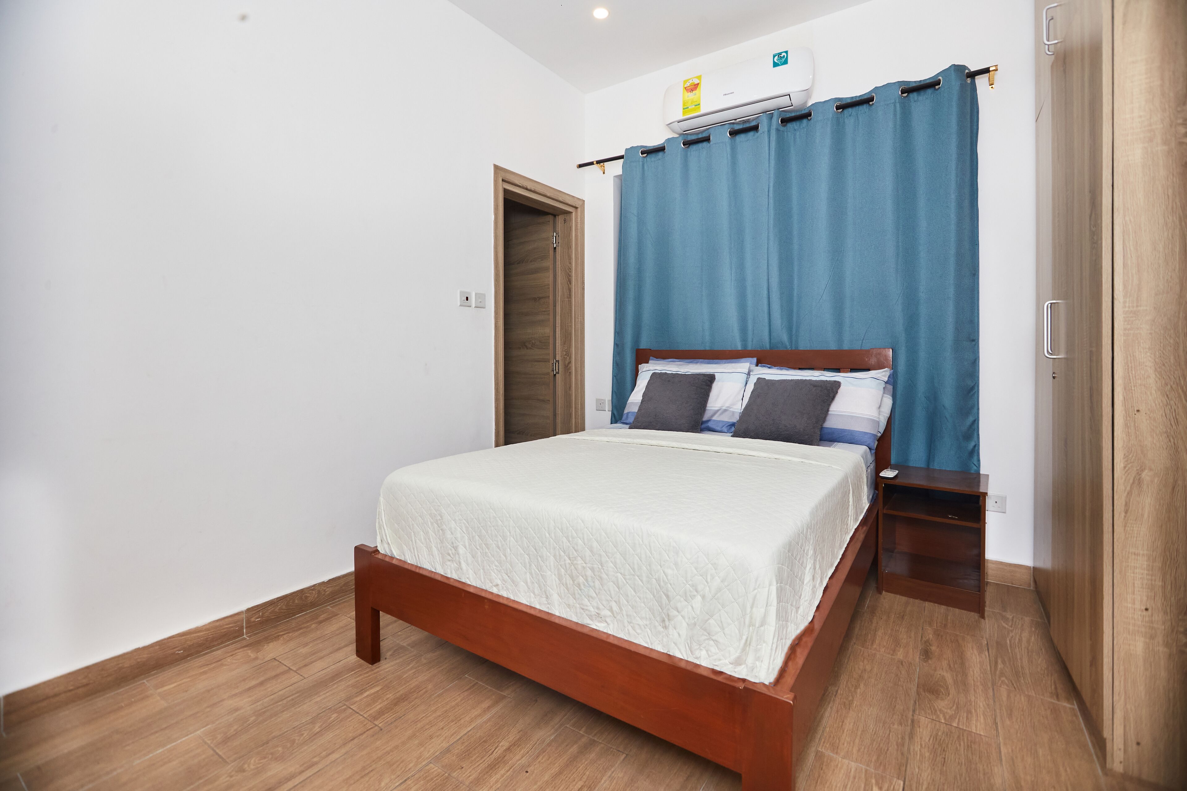 A bedroom with a wooden bed, a nightstand, a blue curtain, and a wooden wardrobe.