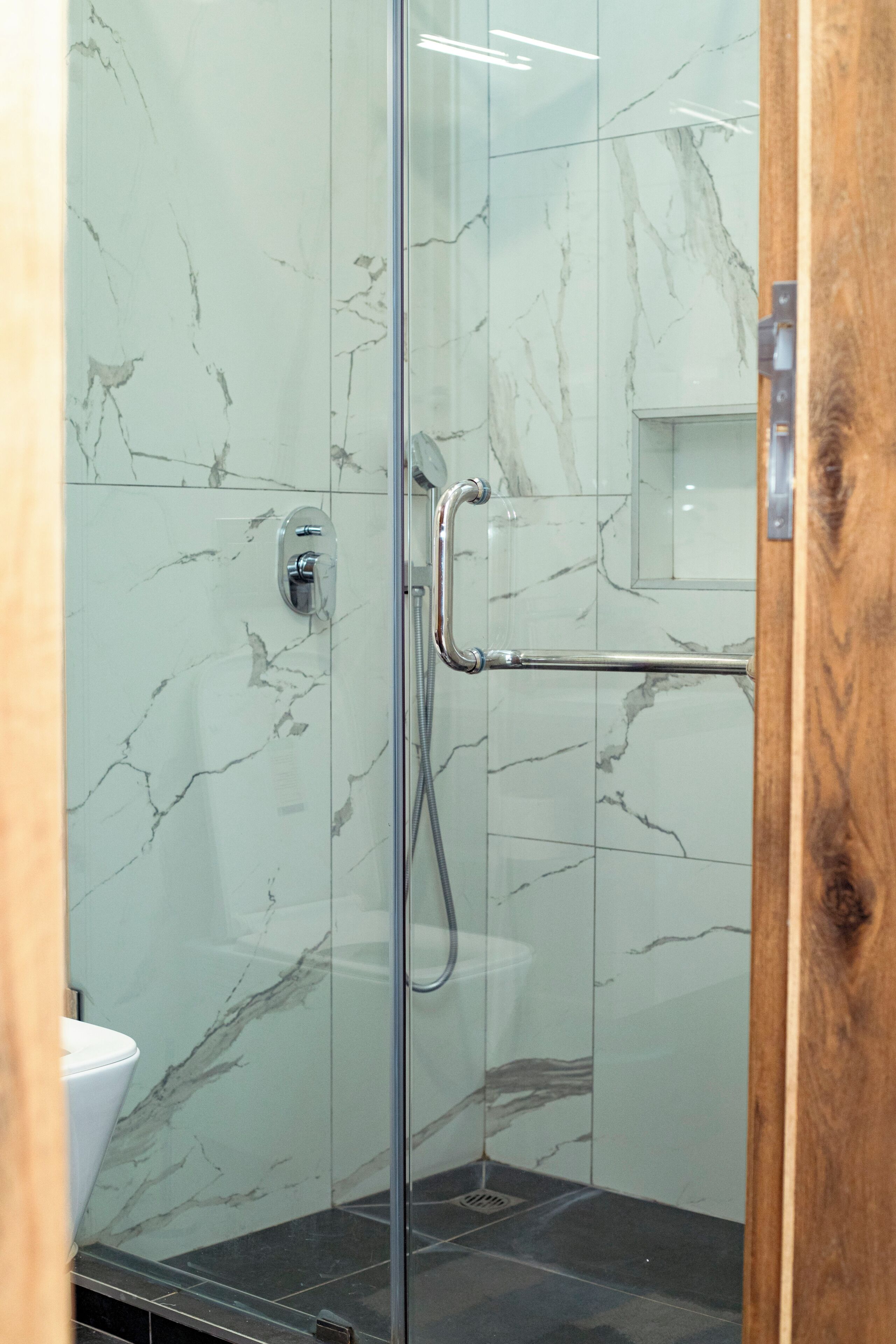 Eine gläserne Dusche mit Marmorwand, Holzrahmen und Handlauf.