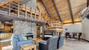 A spacious living area with a stone fireplace, a television, and a piano. - Moose Tracks Cabin! Secluded Mtn Retreat w/HotTub (Woodland Park)