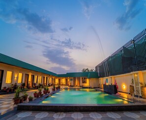 Un patio de hotel con piscina, plantas en macetas y un edificio con techo verde.