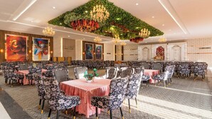 Un amplio salón de banquetes con decoraciones florales en el techo, múltiples candelabros y una fila de mesas con manteles florales.