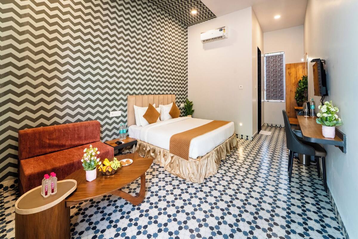 A hotel room with a bed, a sofa, a small table with a vase of flowers, and a TV.