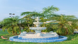 Una fuente de varios niveles con base de azulejos, rodeada de palmeras y césped.