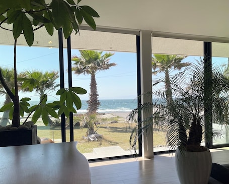A room with large windows overlooking a beach, palm trees, and the ocean.