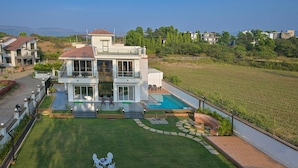 A modern two-story house with a swimming pool, a well-maintained lawn, and a view of the surrounding landscape. - Vivanta Villa (Mawal)