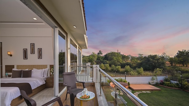 A balcony with a bed, chairs, and a table with snacks. - Vivanta Villa (Mawal)