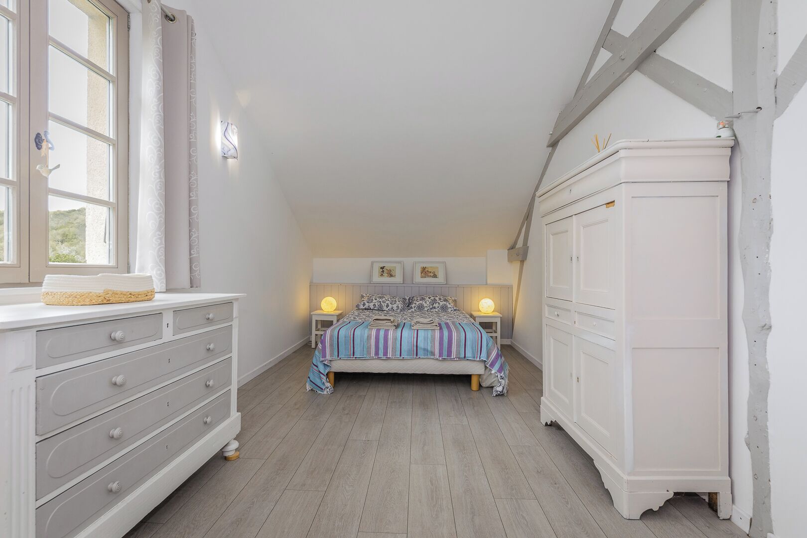 Een slaapkamer met een bed, nachtlampjes, een dressoir en een kledingkast.