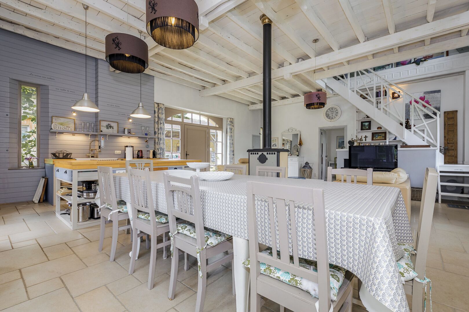 Een ruime keuken met een eethoek, met een lange tafel, witte stoelen en hanglampen.
