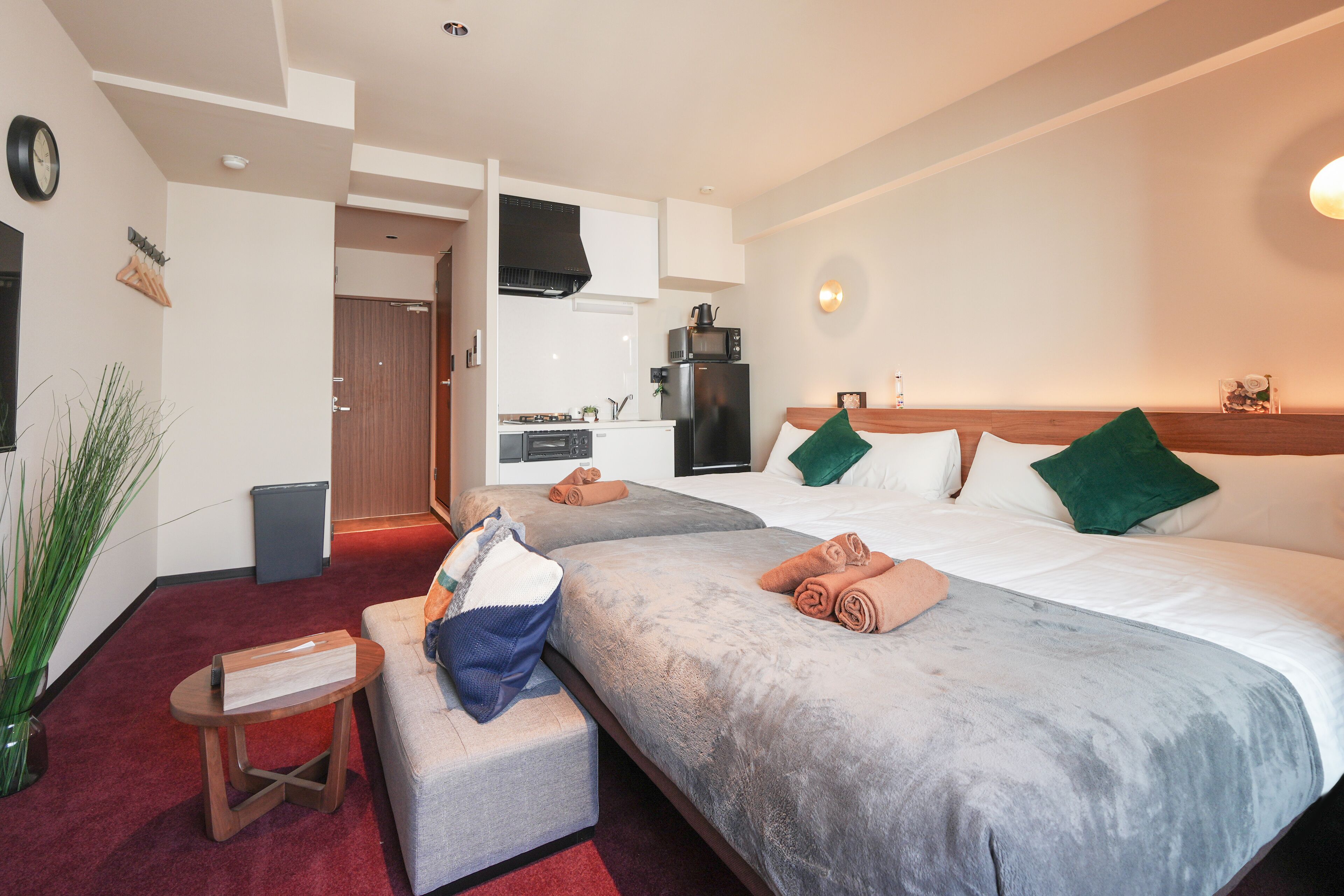 A hotel room with two beds, a small kitchenette, a seating area with a table, and a potted plant.